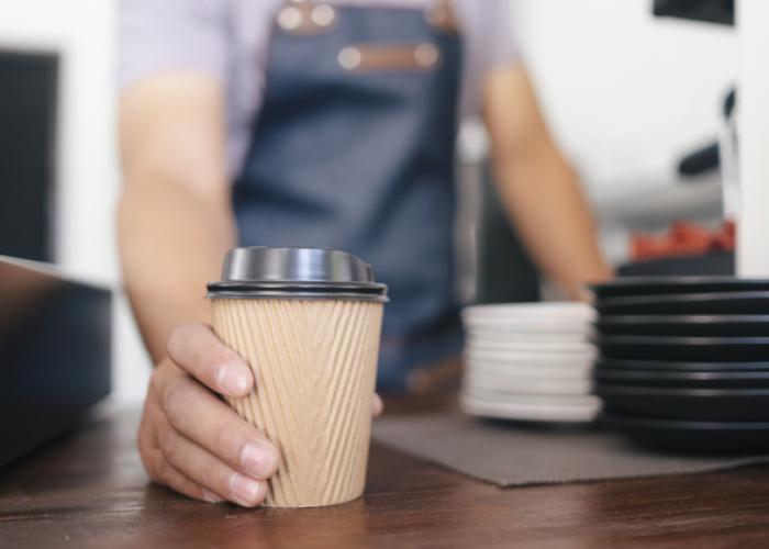 man with to go coffee in disposable cup on countertop