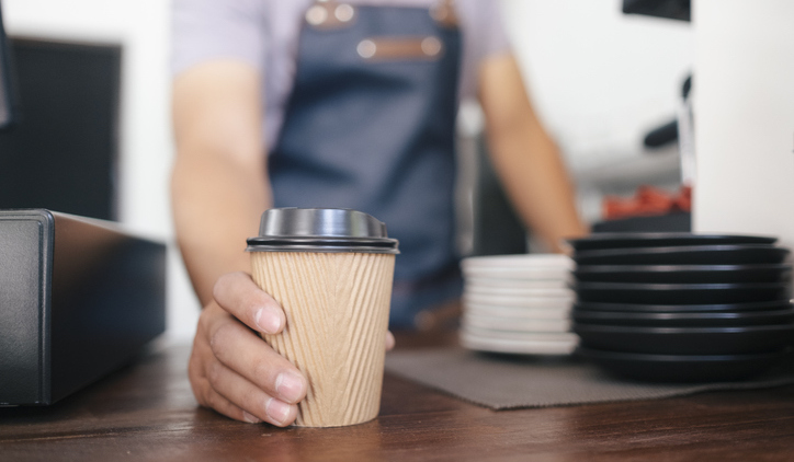 man with to go coffee in disposable cup on countertop